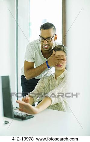 Man covering colleague's eyes in office View Large Photo Image Stock Photo - Man covering colleague's eyes in office. Fotosearch