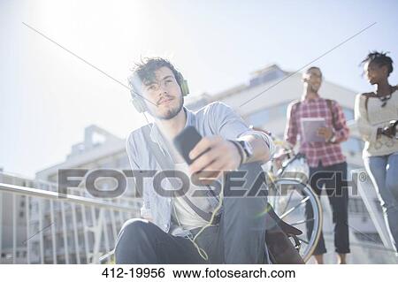 Man listening to headphones on city street View Large Photo Image Stock Photograph - Man listening to headphones on city street. Fotosearch