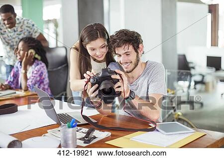 Stock Image - People reviewing photos together in office. Fotosearch