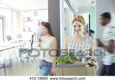 Stock Image - Woman carrying cardboard box in office. Fotosearch