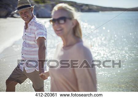 Stock Image - Couple holding hands on beach. Fotosearch