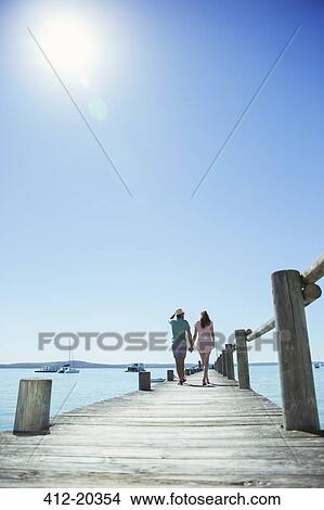 Couple holding hands walking along wooden dock View Large Photo Image Picture - Couple holding hands walking along wooden dock. Fotosearch