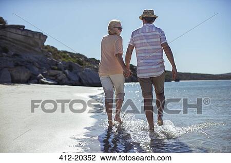 Couple holding hands walking along shore View Large Photo Image Stock Image - Couple holding hands walking along shore. Fotosearch