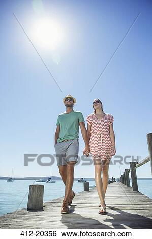 Couple holding hands walking along wooden dock View Large Photo Image Stock Photograph - Couple holding hands walking along wooden dock. Fotosearch