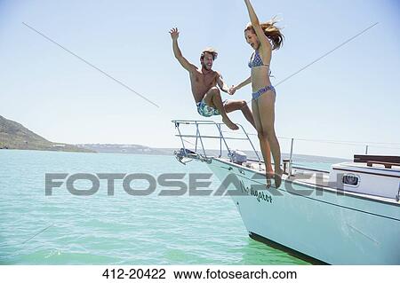 Stock Image - Couple jumping off boat together . Fotosearch