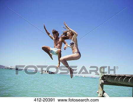 Stock Image - Couple jumping off wooden dock together . Fotosearch