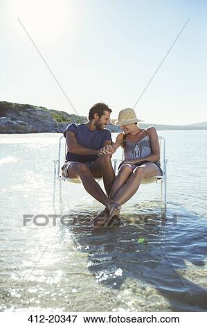 Stock Photo - Couple sitting in chairs in waves . Fotosearch