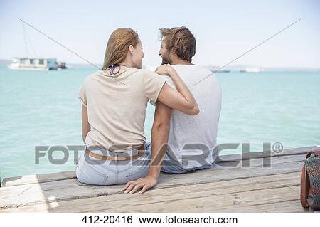 Stock Photograph - Couple sitting on edge of wooden dock together . Fotosearch