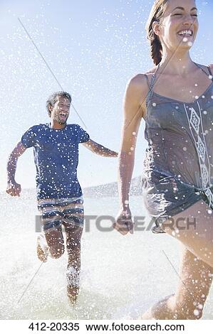 Stock Photography - Couple splashing in water on beach. Fotosearch