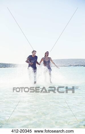 Stock Photography - Couple splashing in water on beach. Fotosearch