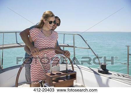 Stock Image - Couple steering sailboat together . Fotosearch