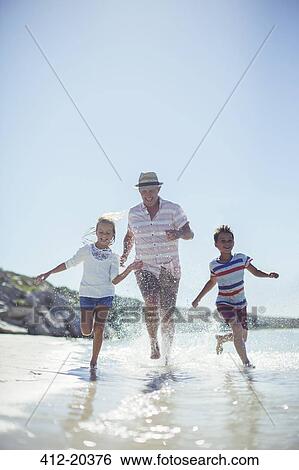 Stock Photograph - Family running in water on beach. Fotosearch