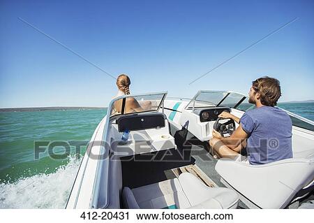 Stock Image - Man steering boat on water with girlfriend. Fotosearch