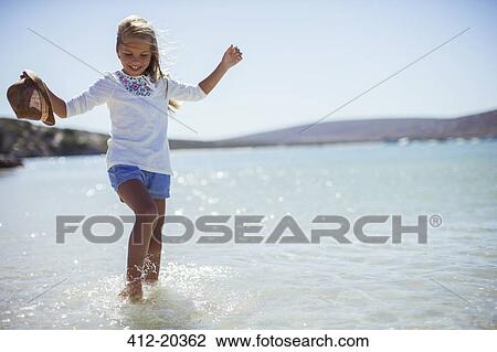 Stock Image - Young girl splashing in water on beach . Fotosearch