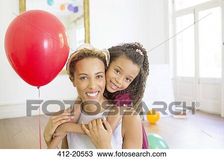 Stock Image - Mother and daughter hugging in living space. Fotosearch