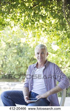 Stock Photograph - Older man sitting with digital tablet outdoors. Fotosearch