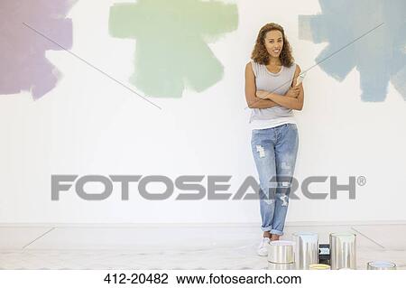 Stock Image - Woman standing between paint swatches on wall . Fotosearch