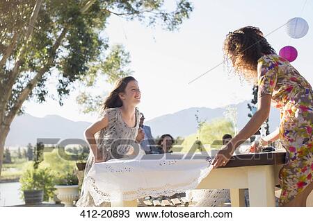 Stock Image - Mother and daughter laying table cloth on table. Fotosearch