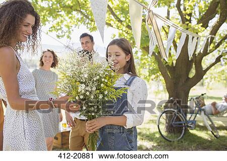 Stock Image - Woman admiring flowers held by young girl . Fotosearch