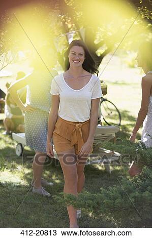 Stock Image - Woman walking through sunny park. Fotosearch