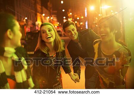 Picture - Friends walking down city street together at night. Fotosearch