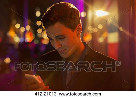 Stock Image - Man using cell phone on city street at night . Fotosearch
