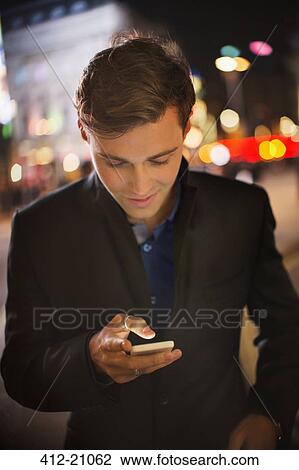 Man using cell phone on city street at night View Large Photo Image Stock Image - Man using cell phone on city street at night. Fotosearch