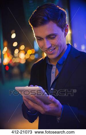Stock Image - Man using digital tablet on city street at night. Fotosearch