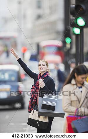Stock Image - Woman hailing taxi on city street . Fotosearch
