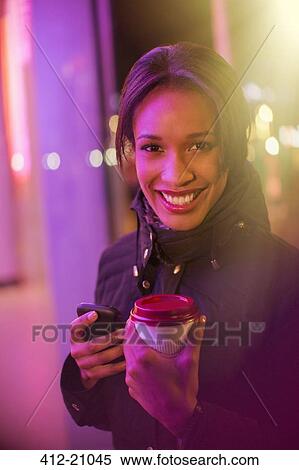 Woman on city street with coffee and cell phone at night View Large Photo Image Stock Photography - Woman on city street with coffee and cell phone at night . Fotosearch
