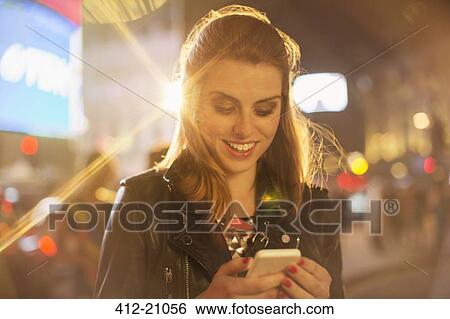Stock Photograph - Woman using cell phone on city street at night. Fotosearch