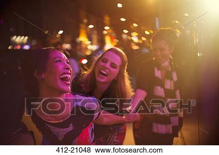 Stock Photo - Women laughing together on city street at night. Fotosearch