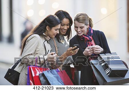 Stock Image - Women looking at cell phone on city street. Fotosearch