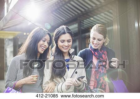 Women looking at cell phone on city street View Large Photo Image Stock Photography - Women looking at cell phone on city street. Fotosearch