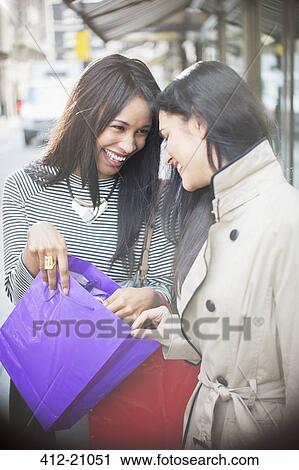 Women looking through shopping bag together on city street View Large Photo Image Stock Image - Women looking through shopping bag together on city street. Fotosearch