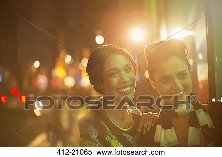 Stock Photography - Women smiling together on city street at night . Fotosearch