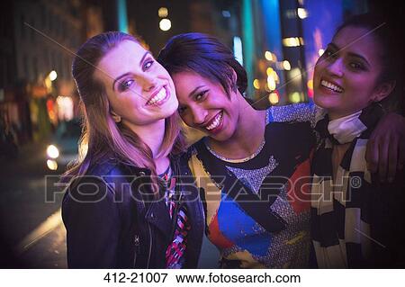 Stock Photo - Women smiling together outside of store at night . Fotosearch