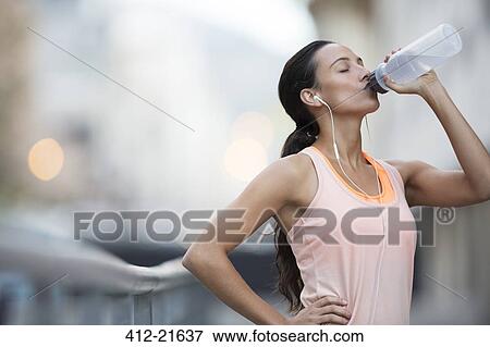 Woman drinking water after exercising on city street View Large Photo Image Stock Photo - Woman drinking water after exercising on city street. Fotosearch