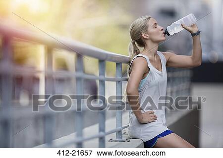 Woman drinking water after exercising on city street View Large Photo Image Stock Photo - Woman drinking water after exercising on city street. Fotosearch