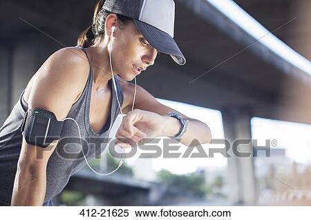 Stock Photography - Woman looking at watch after exercising on city street. Fotosearch