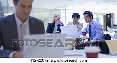 Stock Image - Business people gathered around laptop in office building. Fotosearch