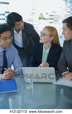 Stock Image - Business people gathered around laptop in office building . Fotosearch