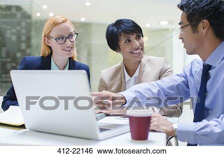 Stock Photograph - Business people gathered around laptop in office building cafe. Fotosearch