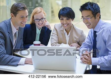 Stock Photograph - Business people gathered around laptop in office building cafe. Fotosearch