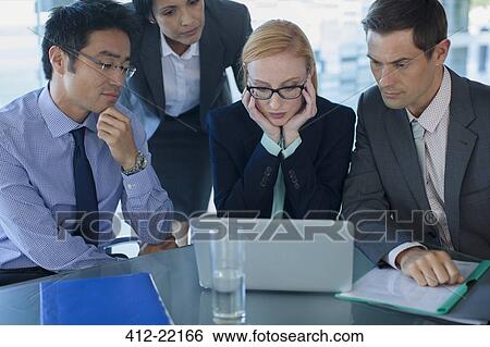 Stock Photograph - Business people gathered around laptop at table in office building. Fotosearch