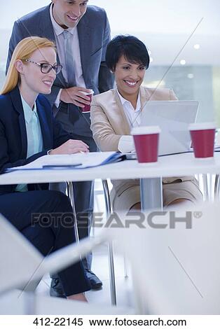 Stock Photography - Business people gathered around laptop in office building cafe. Fotosearch