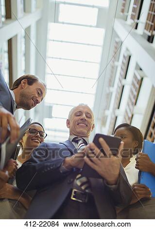 Business people looking at digital tablet in office lobby View Large Photo Image Picture - Business people looking at digital tablet in office lobby. Fotosearch