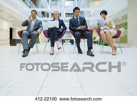 Stock Image - Business people sat in chairs working in office building. Fotosearch