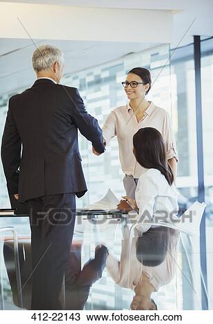 Stock Image - Business people shaking hands in office building. Fotosearch