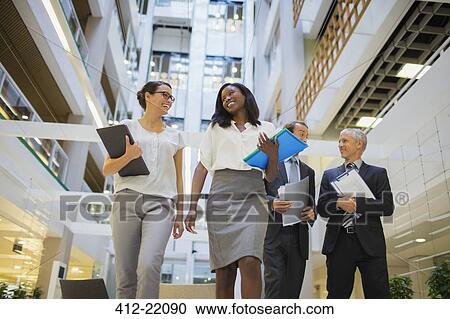 Stock Image - Business people walking together in office building. Fotosearch